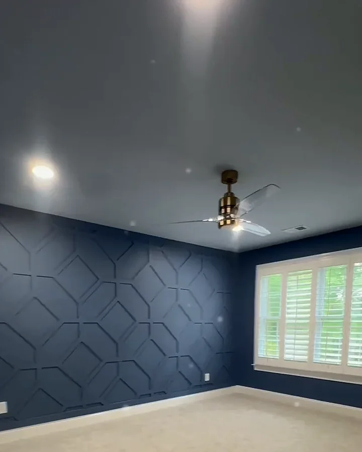 Bedroom with a navy geometric accent wall, blue walls and plantation shutters
